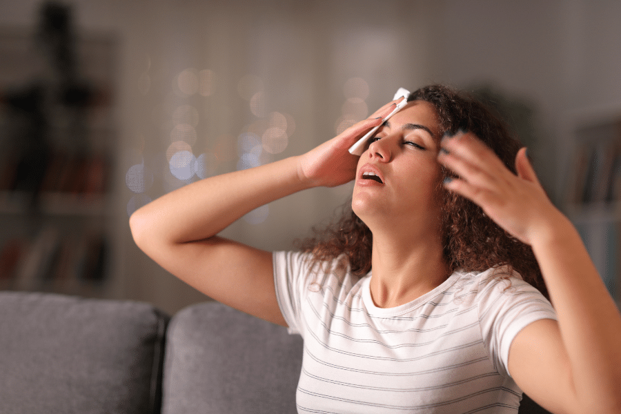 Middle-aged woman fanning herself and looking flushed, experiencing a hot flush due to perimenopause.